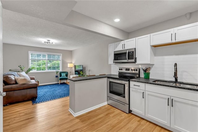 1509 W 25th Ct Unit A2, Lawrence, KS 66046 - kitchen with stainless steel appliances, open floor plan, a peninsula, light wood-type flooring, and white cabinetry