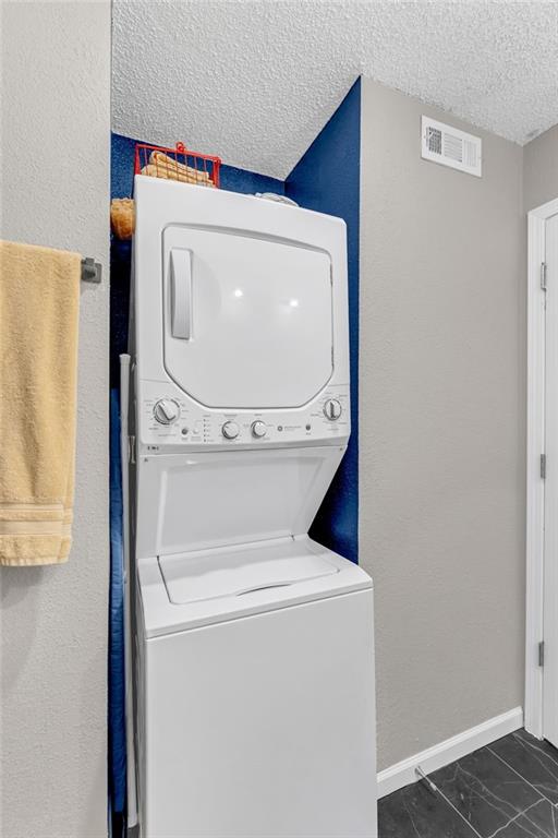 1509 W 25th Ct Unit A2, Lawrence, KS 66046 - washroom featuring stacked washer and clothes dryer, a textured ceiling, and marble finish flooring