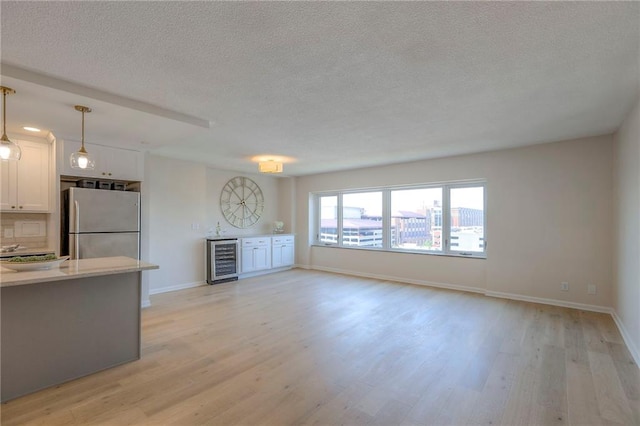 4545 Wornall Rd Unit 1009, Kansas City, MO 64111 - unfurnished living room featuring beverage cooler, light wood-style floors, a textured ceiling, and a dry bar