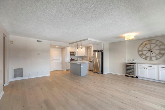 4545 Wornall Rd Unit 1009, Kansas City, MO 64111 - unfurnished living room featuring beverage cooler, a textured ceiling, light wood-style floors, and a dry bar