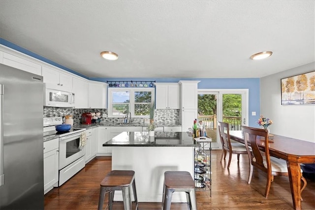 13500 Spring St, Grandview, MO 64030 - kitchen with white appliances, a kitchen bar, healthy amount of natural light, dark wood finished floors, and a textured ceiling