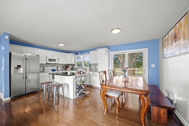 13500 Spring St, Grandview, MO 64030 - kitchen featuring white appliances, dark wood finished floors, white cabinets, backsplash, and a center island