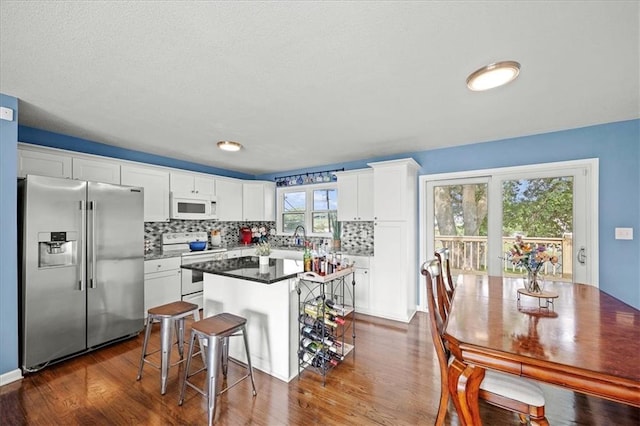 13500 Spring St, Grandview, MO 64030 - kitchen featuring white appliances, white cabinets, a kitchen island, dark wood-style floors, and tasteful backsplash