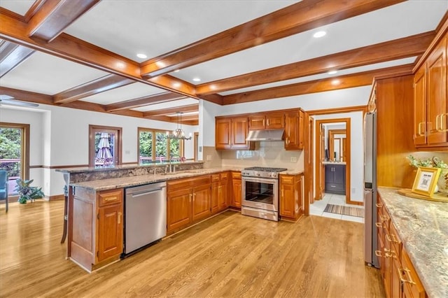 22810 SW Hampton Ct, Blue Springs, MO 64015 - kitchen featuring stainless steel appliances, under cabinet range hood, light wood-style flooring, brown cabinetry, and beam ceiling
