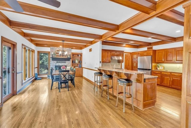 22810 SW Hampton Ct, Blue Springs, MO 64015 - kitchen featuring freestanding refrigerator, light wood-style floors, under cabinet range hood, beamed ceiling, and a breakfast bar area