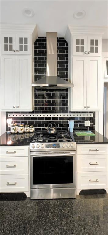 615 N Jefferson St, Carrollton, MO 64633 - kitchen featuring stainless steel range with gas cooktop, wall chimney range hood, white cabinets, and dark stone counters