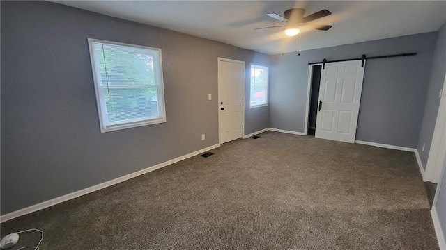 4216 E 67th Ter, Kansas City, MO 64132 - unfurnished bedroom featuring a barn door, dark colored carpet, and ceiling fan