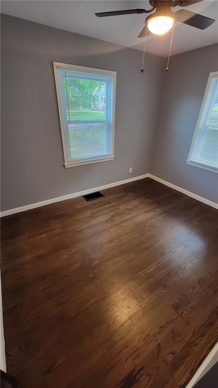 4216 E 67th Ter, Kansas City, MO 64132 - unfurnished room featuring ceiling fan, healthy amount of natural light, and dark wood-style floors