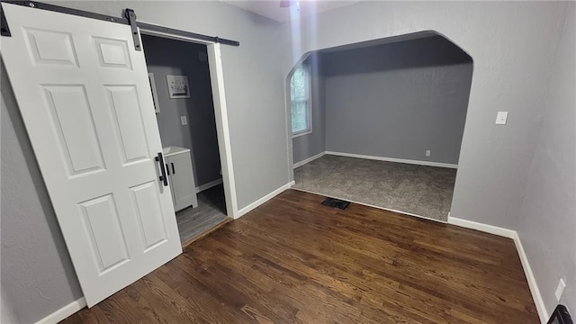 4216 E 67th Ter, Kansas City, MO 64132 - unfurnished room featuring arched walkways, dark wood-type flooring, and a barn door
