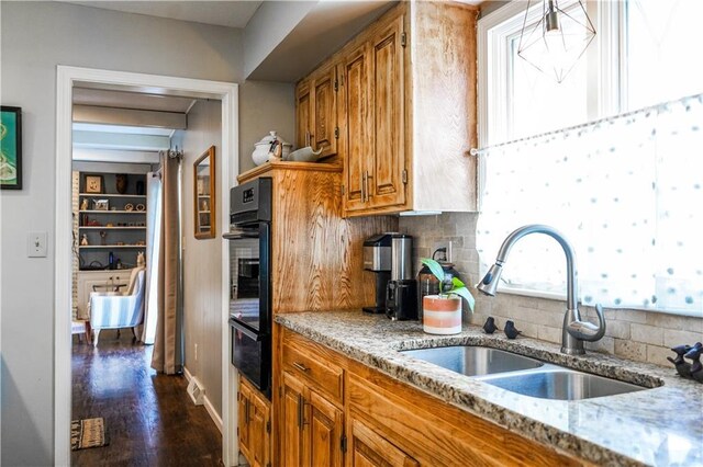 1902 Snowdrop Cir, Liberty, MO 64068 - kitchen featuring black oven, brown cabinetry, light stone counters, decorative backsplash, and a warming drawer