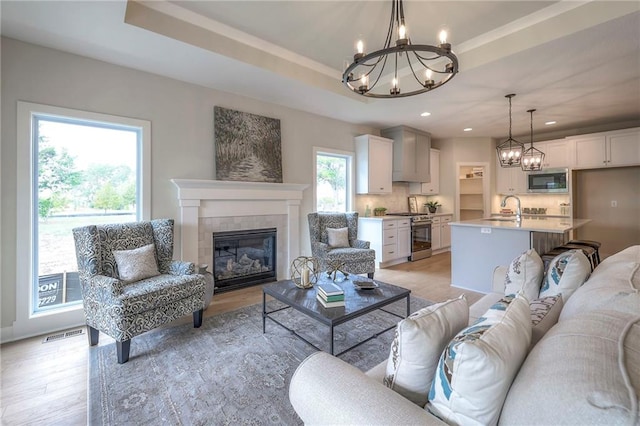 24110 W 95th St, Lenexa, KS 66227 - living area featuring a chandelier, a tiled fireplace, light wood-style floors, recessed lighting, and a tray ceiling