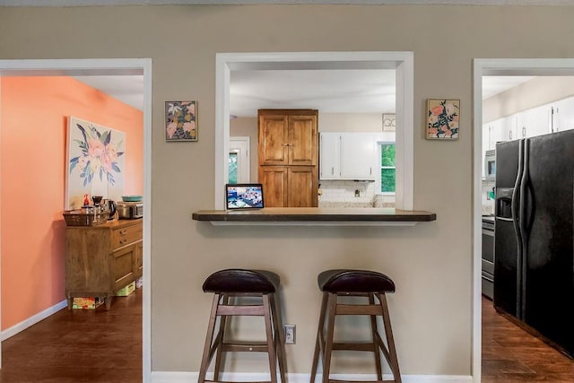 709 S 9th St, Louisburg, KS 66053 - kitchen featuring black refrigerator with ice dispenser, white microwave, a kitchen bar, and dark wood-type flooring