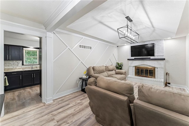 3005 Elmira Ct, Independence, MO 64057 - living area with light wood-type flooring, a brick fireplace, a textured ceiling, and a chandelier