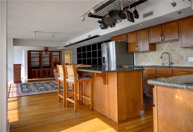 600 Admiral Blvd Unit 1505, Kansas City, MO 64106 - kitchen featuring stainless steel refrigerator with ice dispenser, light wood-style floors, a kitchen bar, brown cabinets, and a center island