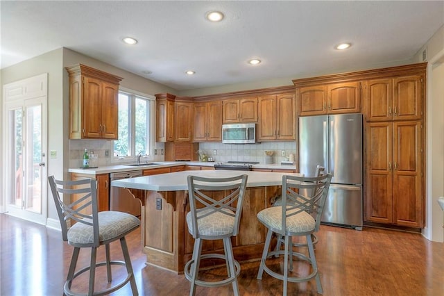 16042 Overbrook Ln, Stilwell, KS 66085 - kitchen with stainless steel appliances, light countertops, dark wood-style flooring, a center island, and brown cabinetry