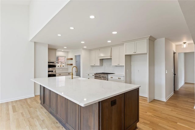 10136 Barton St, Overland Park, KS 66214 - kitchen featuring premium range hood, light wood finished floors, stainless steel appliances, a large island with sink, and white cabinets