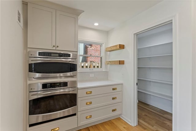 10136 Barton St, Overland Park, KS 66214 - kitchen with stainless steel double oven, light wood-style flooring, light countertops, open shelves, and recessed lighting