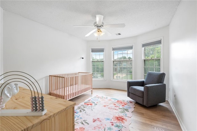 14712 Woodward St, Overland Park, KS 66223 - bedroom with a textured ceiling, wood finished floors, ceiling fan, and a nursery area