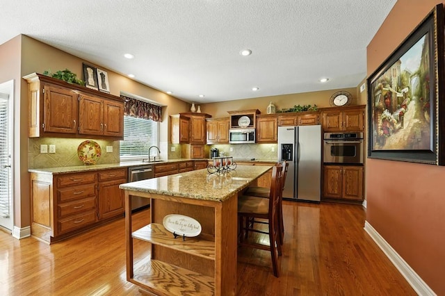 2312 NE Sweet Water Dr, Lees Summit, MO 64086 - kitchen featuring stainless steel appliances, brown cabinets, wood finished floors, decorative backsplash, and a breakfast bar area