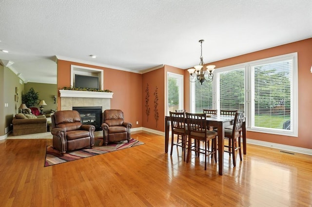 2312 NE Sweet Water Dr, Lees Summit, MO 64086 - dining space featuring a chandelier, a fireplace, light wood-style flooring, crown molding, and a textured ceiling