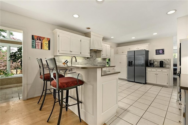 490 W 49th Ter, Kansas City, MO 64112 - kitchen with refrigerator with ice dispenser, a peninsula, backsplash, white cabinetry, and a breakfast bar