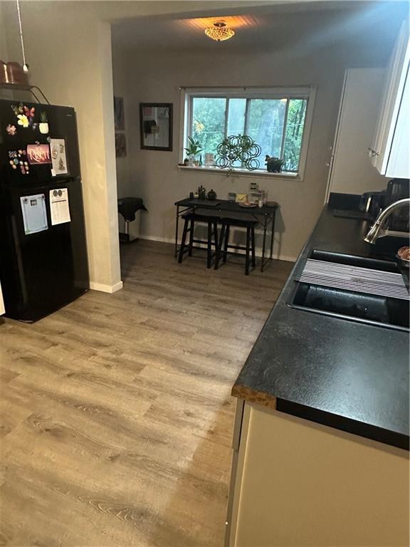 3823 Ruby Ave, Kansas City, KS 66106 - kitchen featuring freestanding refrigerator, light wood-style flooring, white cabinetry, and dark countertops