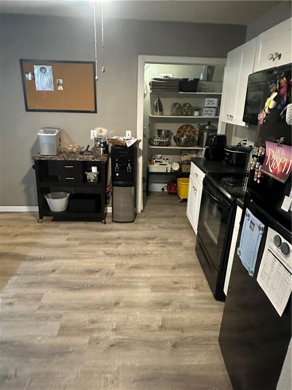 3823 Ruby Ave, Kansas City, KS 66106 - kitchen with black range with electric cooktop, white cabinets, light wood-type flooring, open shelves, and dark countertops