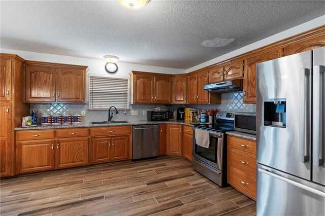 606 S Thornton St, Richmond, MO 64085 - kitchen with stainless steel appliances, under cabinet range hood, wood finished floors, brown cabinetry, and a textured ceiling
