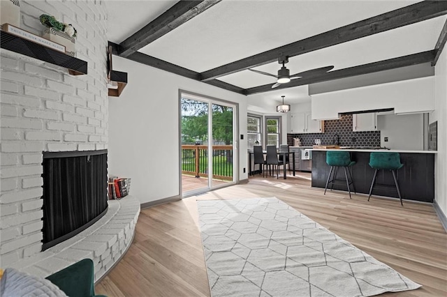 1208 SW Speas Dr, Blue Springs, MO 64014 - living area with light wood finished floors, a brick fireplace, beamed ceiling, and a ceiling fan