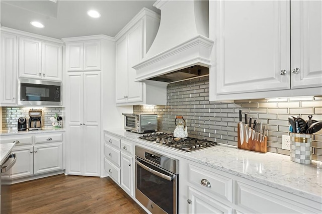 27181 W 100th Ter, Olathe, KS 66061 - kitchen featuring appliances with stainless steel finishes, custom range hood, white cabinets, tasteful backsplash, and light stone counters