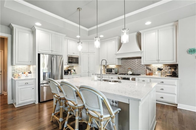 27181 W 100th Ter, Olathe, KS 66061 - kitchen with stainless steel appliances, custom exhaust hood, decorative backsplash, a kitchen island with sink, and white cabinetry