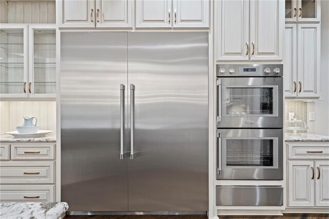 18405 371st Hwy, Platte City, MO 64079 - kitchen with stainless steel appliances, a warming drawer, glass insert cabinets, light stone counters, and white cabinetry