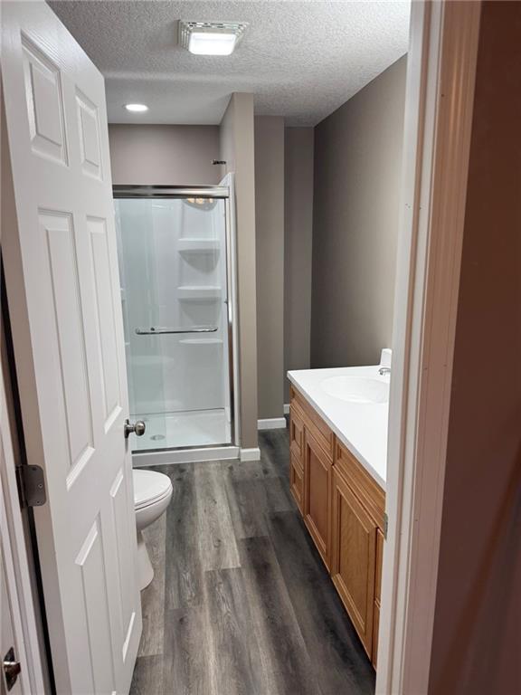 915 Des Moines St, Burlington, KS 66839 - bathroom featuring a shower stall, vanity, wood finished floors, and a textured ceiling