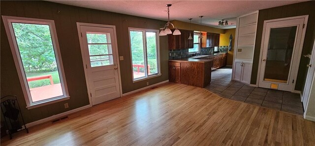 1113 W 27th St, Lawrence, KS 66046 - kitchen featuring wood finished floors, tasteful backsplash, pendant lighting, and a peninsula