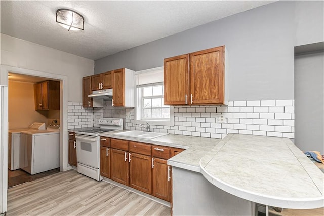 4429 Wabash Ave, Kansas City, MO 64130 - kitchen with white range with electric stovetop, washer and clothes dryer, under cabinet range hood, light wood-style flooring, and a textured ceiling