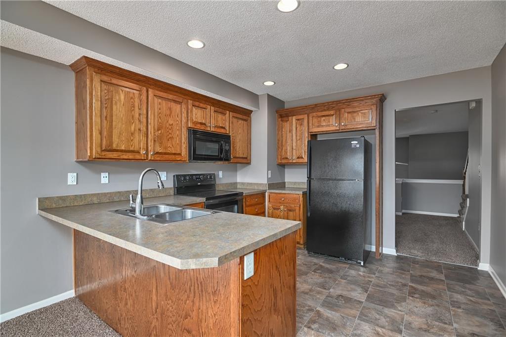 1843 W Spruce St, Olathe, KS 66061 - kitchen with black appliances, brown cabinetry, a peninsula, a textured ceiling, and recessed lighting