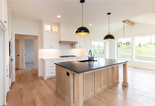 18505 Mohawk Ln, Overland Park, KS 66085 - kitchen with light wood-style flooring, decorative backsplash, dark countertops, an island with sink, and glass insert cabinets