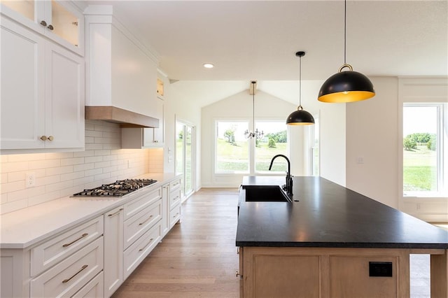 18505 Mohawk Ln, Overland Park, KS 66085 - kitchen with stainless steel gas stovetop, light wood-type flooring, a kitchen island with sink, tasteful backsplash, and white cabinets