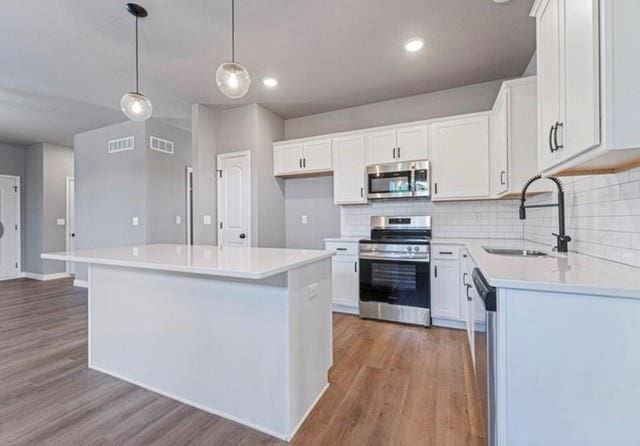 12508 S Parkwood Ln, Lees Summit, MO 64086 - kitchen with appliances with stainless steel finishes, decorative backsplash, wood finished floors, white cabinetry, and recessed lighting