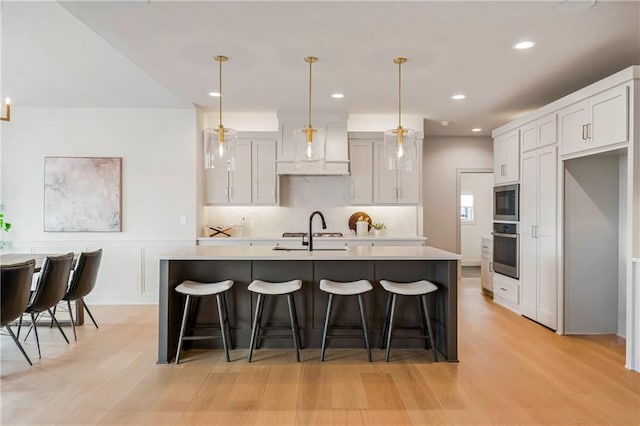 12400 W 184th St, Overland Park, KS 66013 - kitchen with appliances with stainless steel finishes, light countertops, light wood-style floors, a kitchen breakfast bar, and a center island with sink