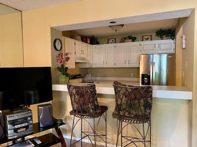 8806 W 106th Ter, Overland Park, KS 66212 - kitchen featuring stainless steel fridge, under cabinet range hood, white cabinets, and a breakfast bar area
