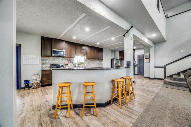 9414 Greenton Rd, Odessa, MO 64076 - kitchen featuring stainless steel microwave, light wood-style floors, a breakfast bar, a textured ceiling, and electric range