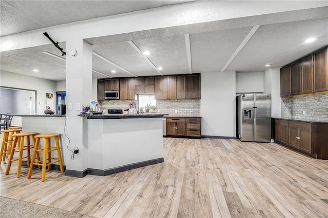 9414 Greenton Rd, Odessa, MO 64076 - kitchen featuring appliances with stainless steel finishes, light wood finished floors, decorative backsplash, a textured ceiling, and a peninsula