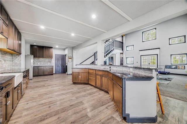 9414 Greenton Rd, Odessa, MO 64076 - kitchen with a kitchen bar, light wood-style flooring, decorative backsplash, dark stone counters, and open floor plan