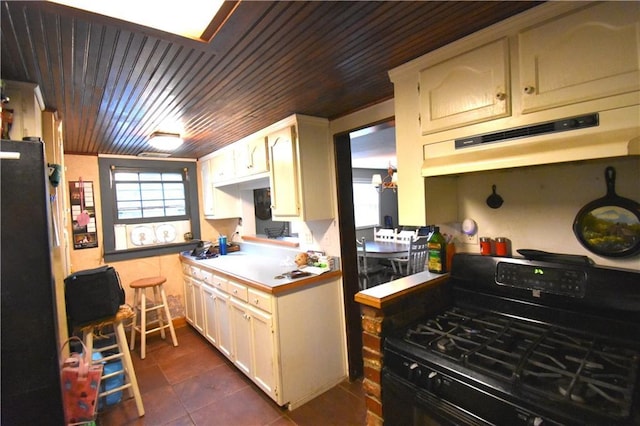 31212 E Webster Rd, Grain Valley, MO 64029 - kitchen with black gas stove, under cabinet range hood, wood ceiling, dark tile patterned floors, and light countertops