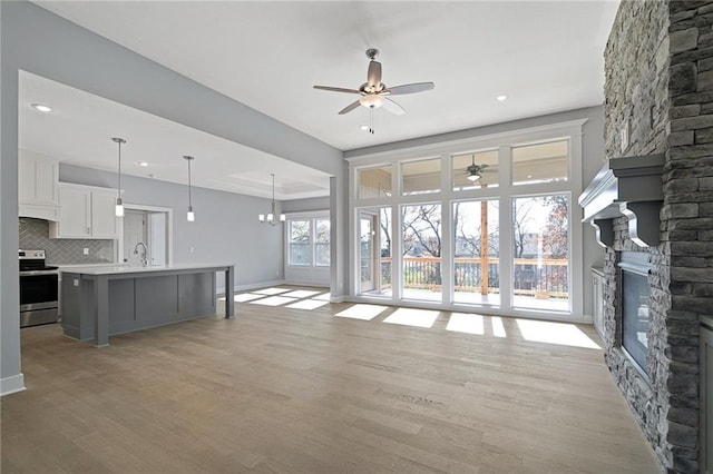 19499 W 114th Ter, Olathe, KS 66061 - unfurnished living room featuring a stone fireplace, ceiling fan, light wood-style floors, recessed lighting, and a chandelier