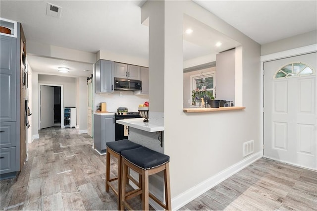 118 Village St, Tonganoxie, KS 66086 - kitchen featuring stainless steel microwave, black electric range oven, gray cabinets, light wood-style flooring, and light countertops