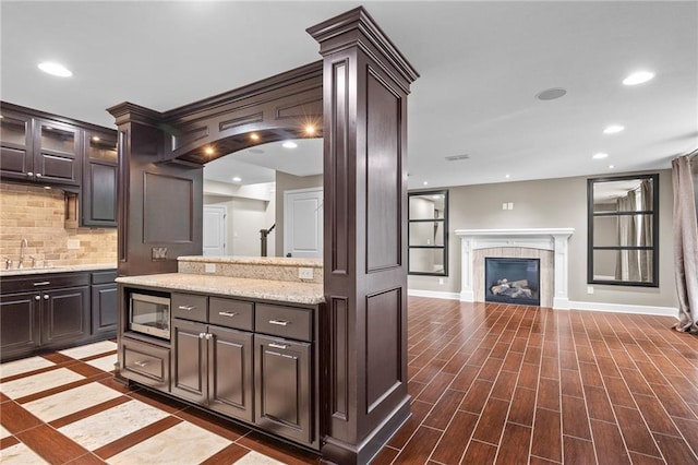 5209 W 161st St, Overland Park, KS 66085 - kitchen featuring backsplash, dark brown cabinetry, stainless steel microwave, recessed lighting, and a glass covered fireplace