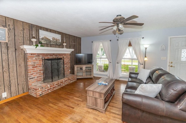 106 S Clark St, Adrian, MO 64720 - living room with wood finished floors, wooden walls, a ceiling fan, and a brick fireplace