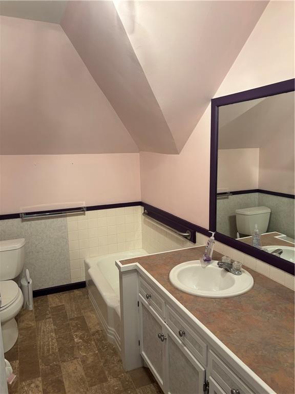 201 W Royle St, Richmond, MO 64085 - bathroom with vaulted ceiling, a bath, vanity, and wainscoting